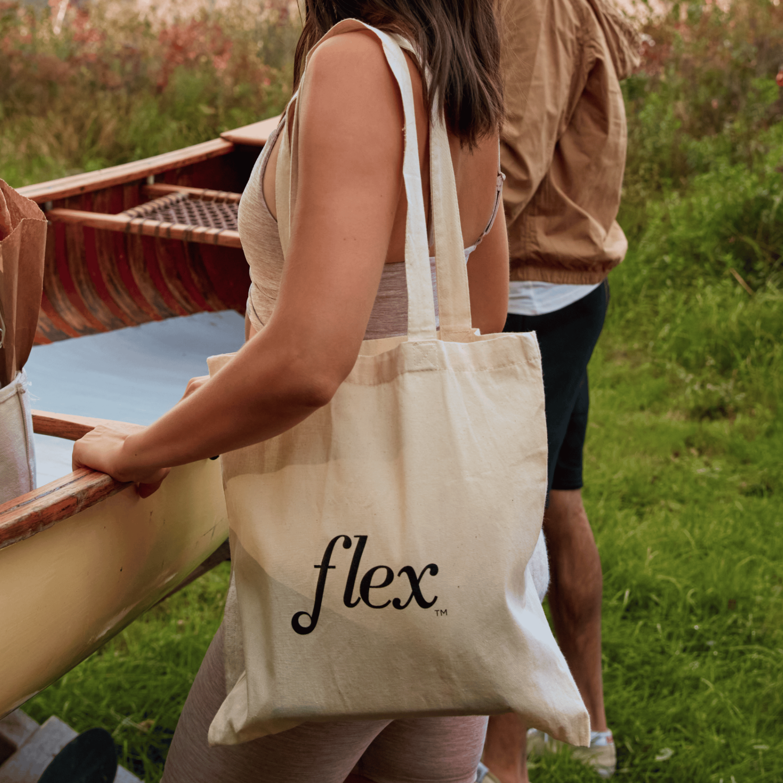 Person carrying a canvas tote bag with Flex logo near a canoe