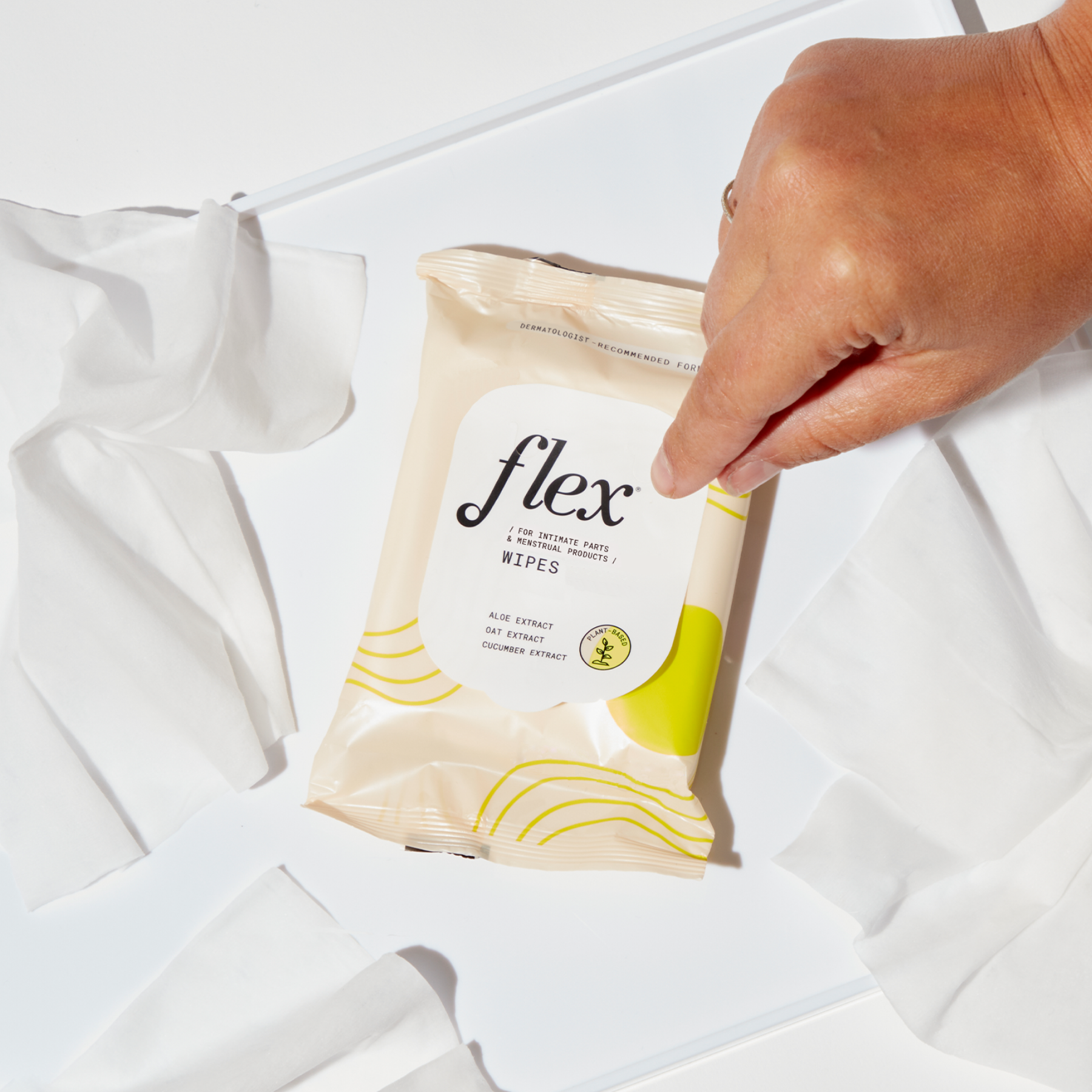 Hand holding a pack of Flex wipes with opened tissues around it