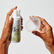 Hands holding a foaming cleanser bottle and a reusable menstrual disc