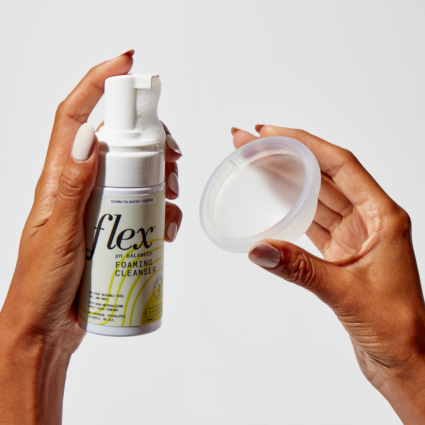 Hands holding a foaming cleanser bottle and a reusable menstrual disc