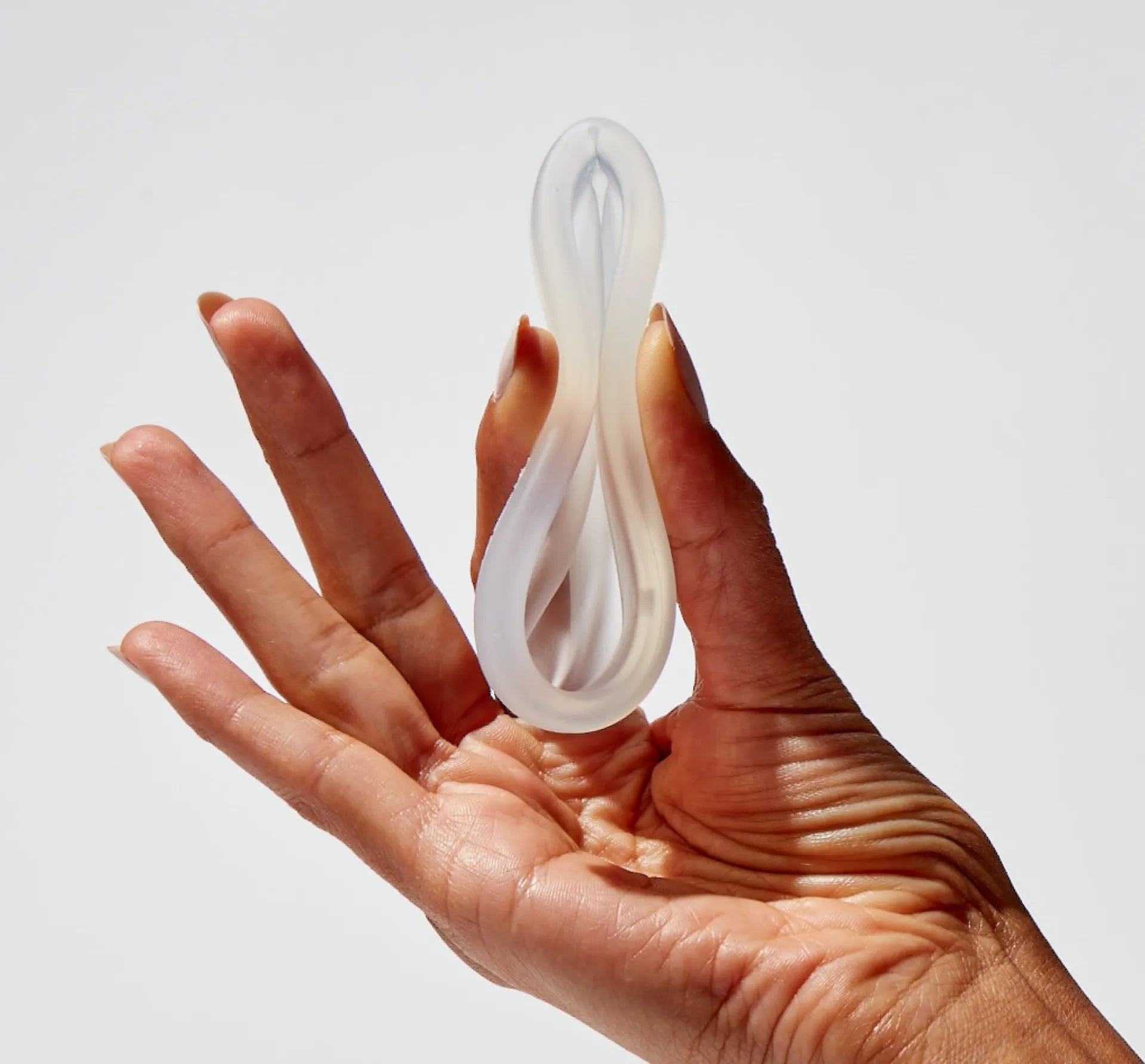Hand holding a folded reusable menstrual disc to show flexibility and insertion method