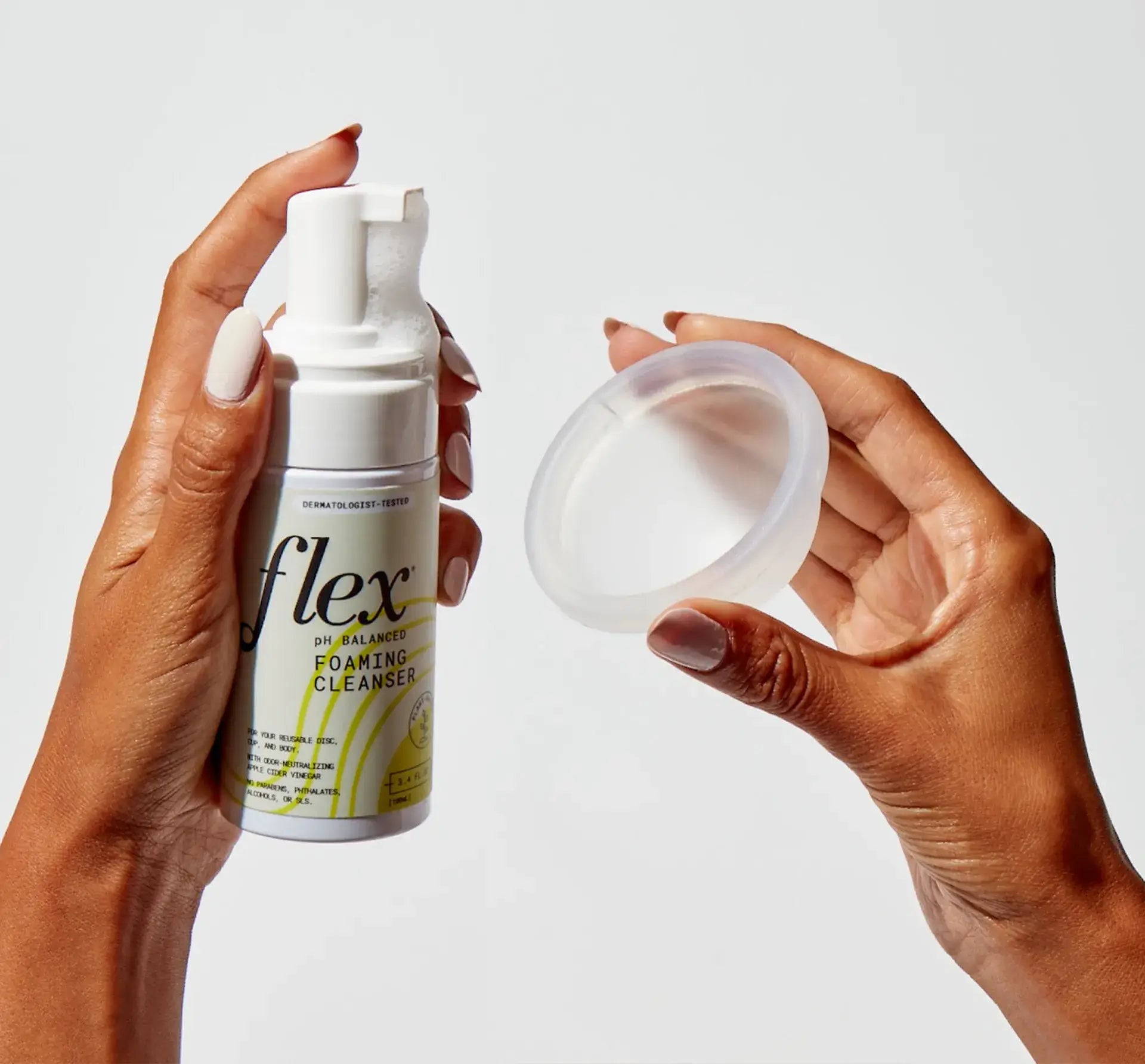 Hands holding a menstrual disc and a bottle of foaming cleanser